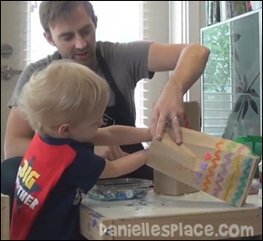 Preschool child using fine motor skills to stuff a bag to make a craft with his father.